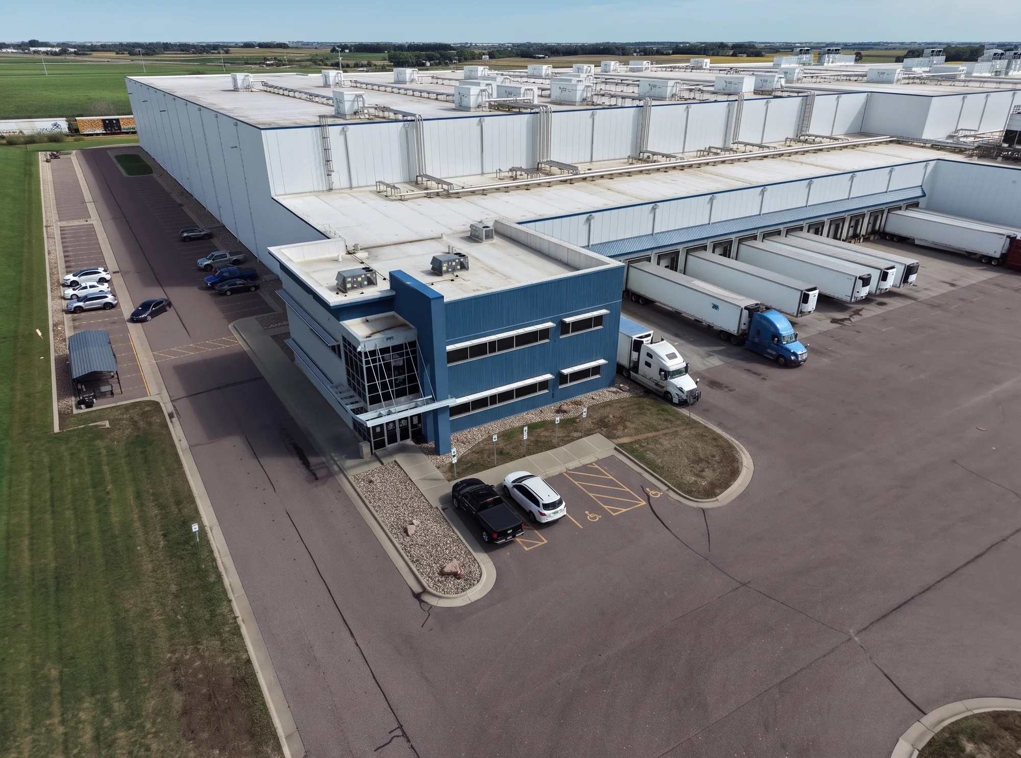 Oblique aerial of the facility: office block, dock doors with refrigerated trailers, and roof units receding toward the horizon